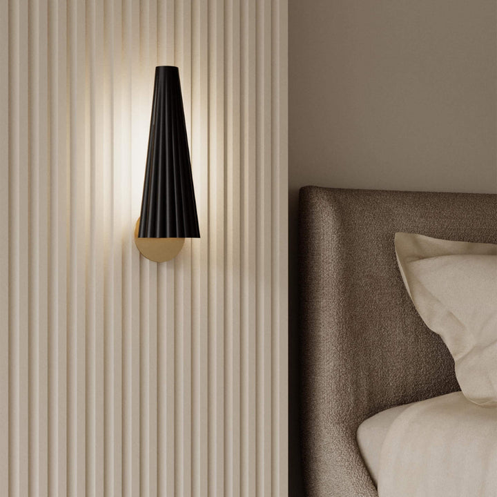 Modern wall lamp with a black and gold design on a beige wall next to a bed.
