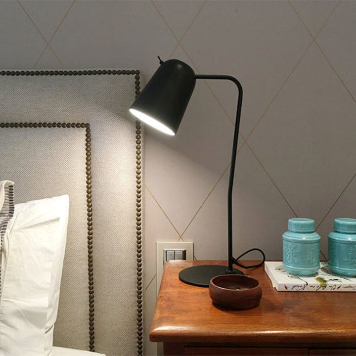 Black desk lamp on a wooden nightstand with decorative items against a gray wall.