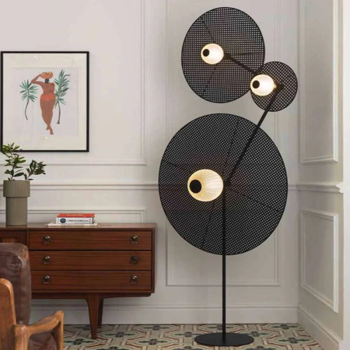 Modern black floor lamp with circular design in a room with a wooden cabinet and decorative items by Bazar Mondiale