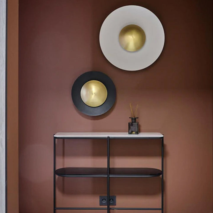 Two round wall lights with gold centers on a brown wall above a black console table.