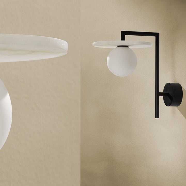 Modern wall-mounted light fixture with black arm and white globe on a beige wall.
