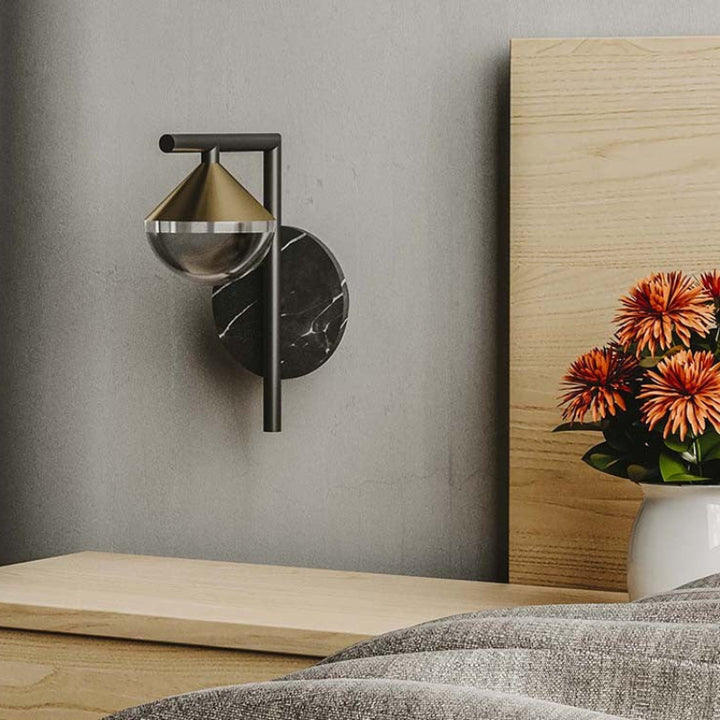 Modern wall sconce on a gray wall with a wooden nightstand and decorative plant.