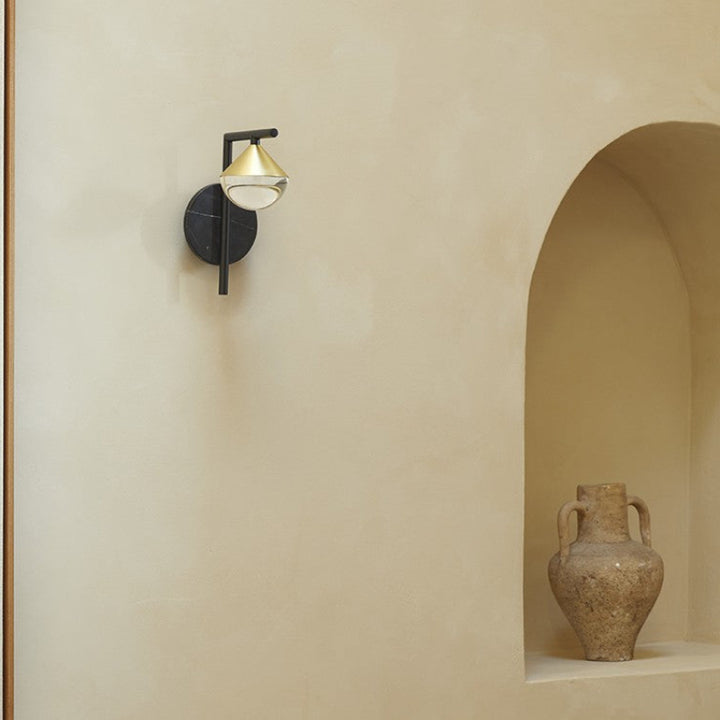Wall sconce with a gold shade on a beige wall next to an abstract painting and a vase.