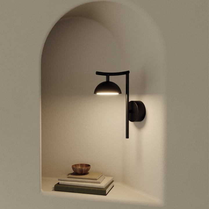 Modern black wall sconce lighting a corner with books and a bowl.