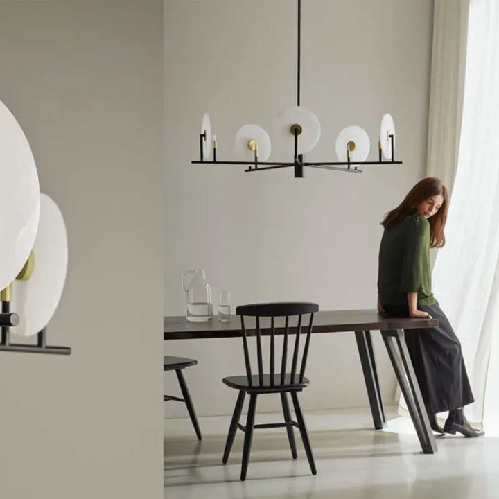 Woman sitting at a dining table in a modern room with a modern chandelier. by Bazar Mondiale