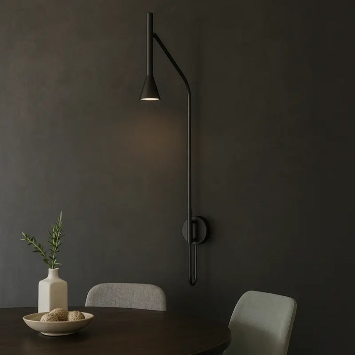 Modern black wall lamp on a dark wall with a table and chairs below by Bazar Mondiale and Aromas Del Campo.