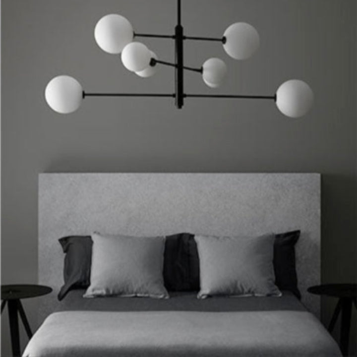 Modern chandelier hanging above a bed in a bedroom with gray walls.